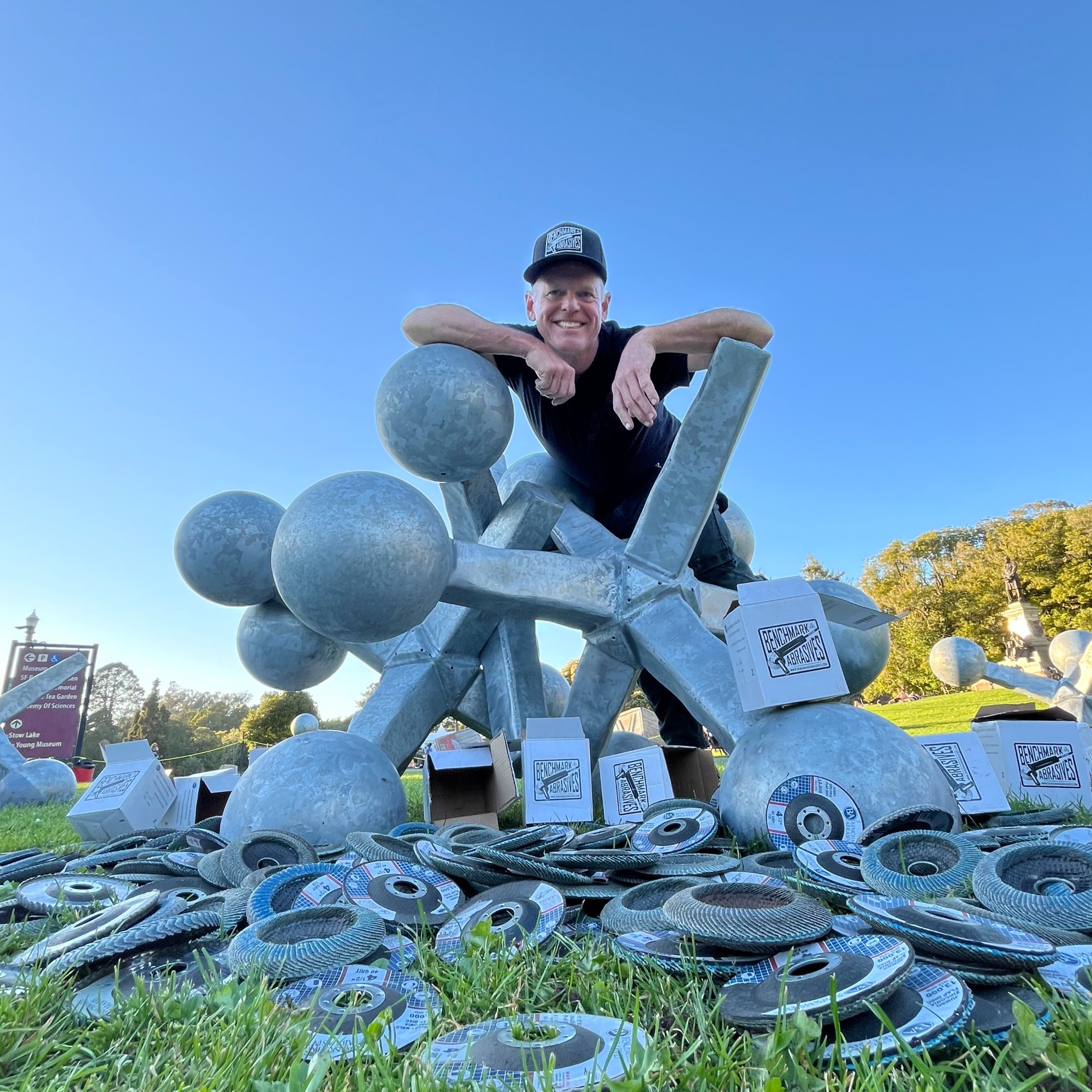 Kevin Byall, co-designer and lead fabricator of Where's the Ball? (The Jax), leans on a jax sculpture surrounded by Benchmark Abrasives supplies at Golden Gate Park, March 2026