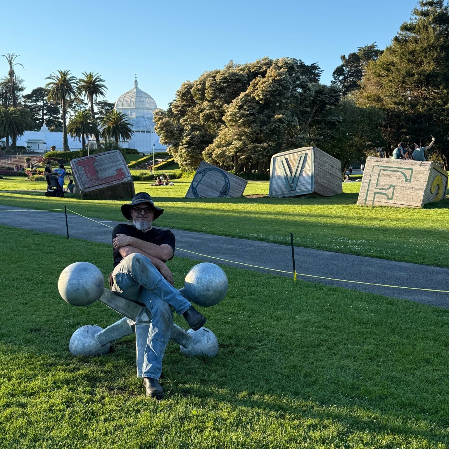 Mark Deem, founder of Misfit Toys Art, seated on one of the steel jax sculptures during installation at the Conservatory of Flowers lawn, Golden Gate Park, March 2026
