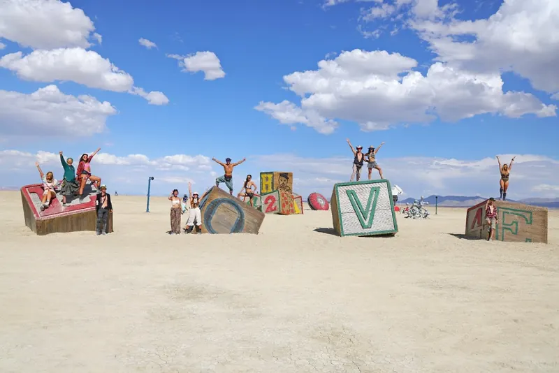 People climbing the giant L-O-V-E blocks of One Tin Soldier at Black Rock City
