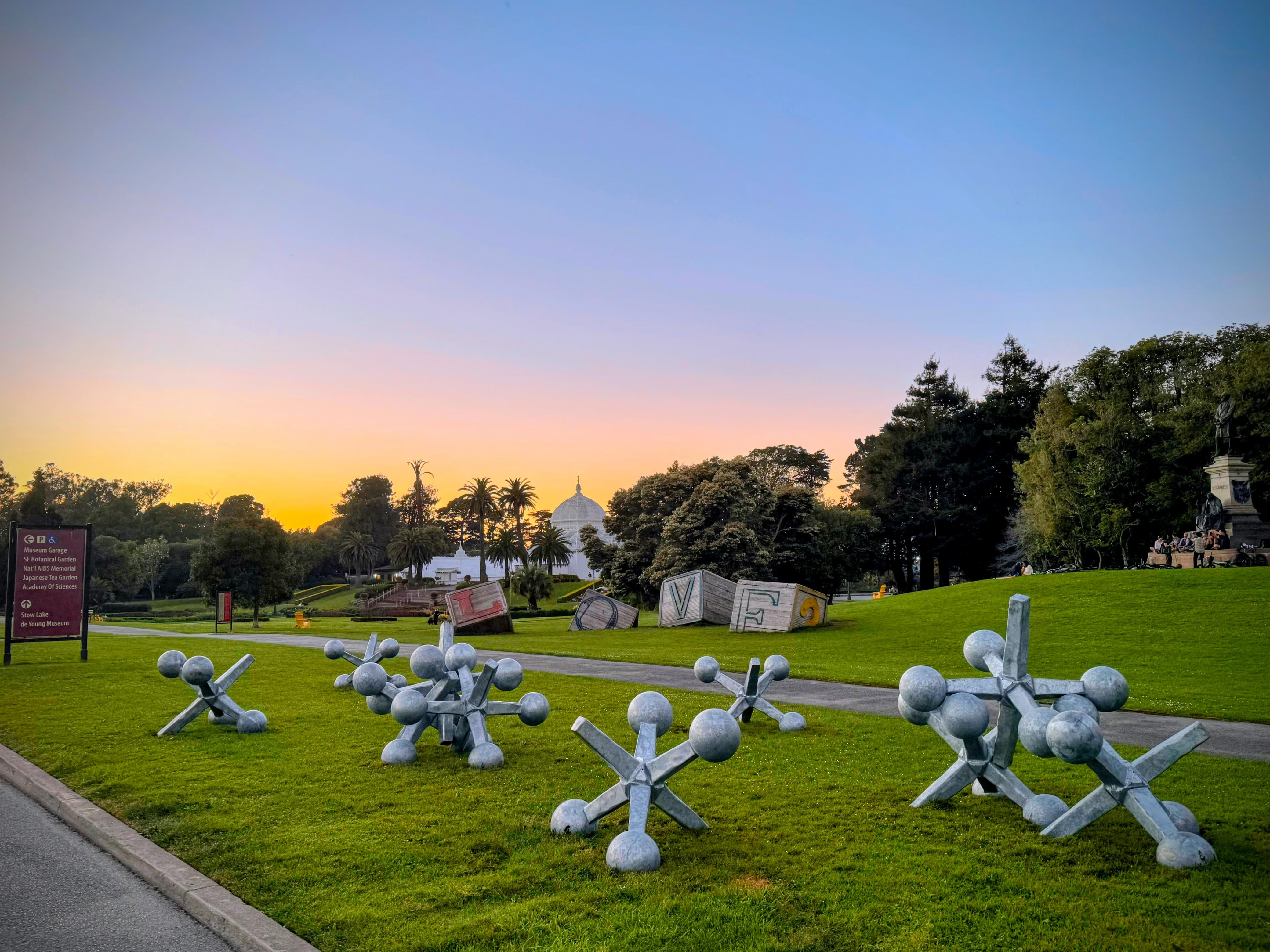 Ten monumental steel jax sculptures scattered across the lawn of the Conservatory of Flowers in Golden Gate Park at sunset, March 2026
